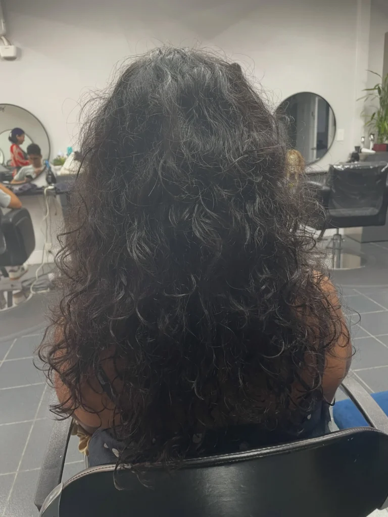 Back view of a Korean wolf cut on long curly hair with layered, textured ends