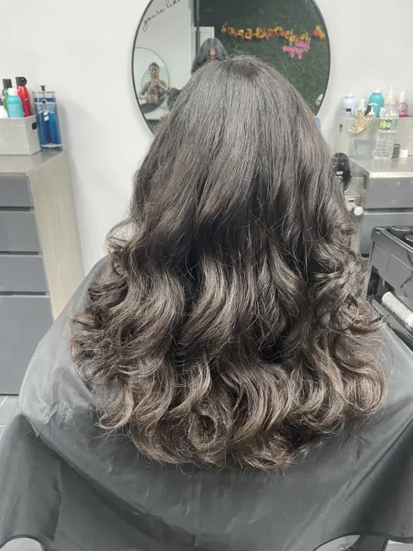 Back view of a woman's long hair styled in a wavy blowout with soft voluminous curls